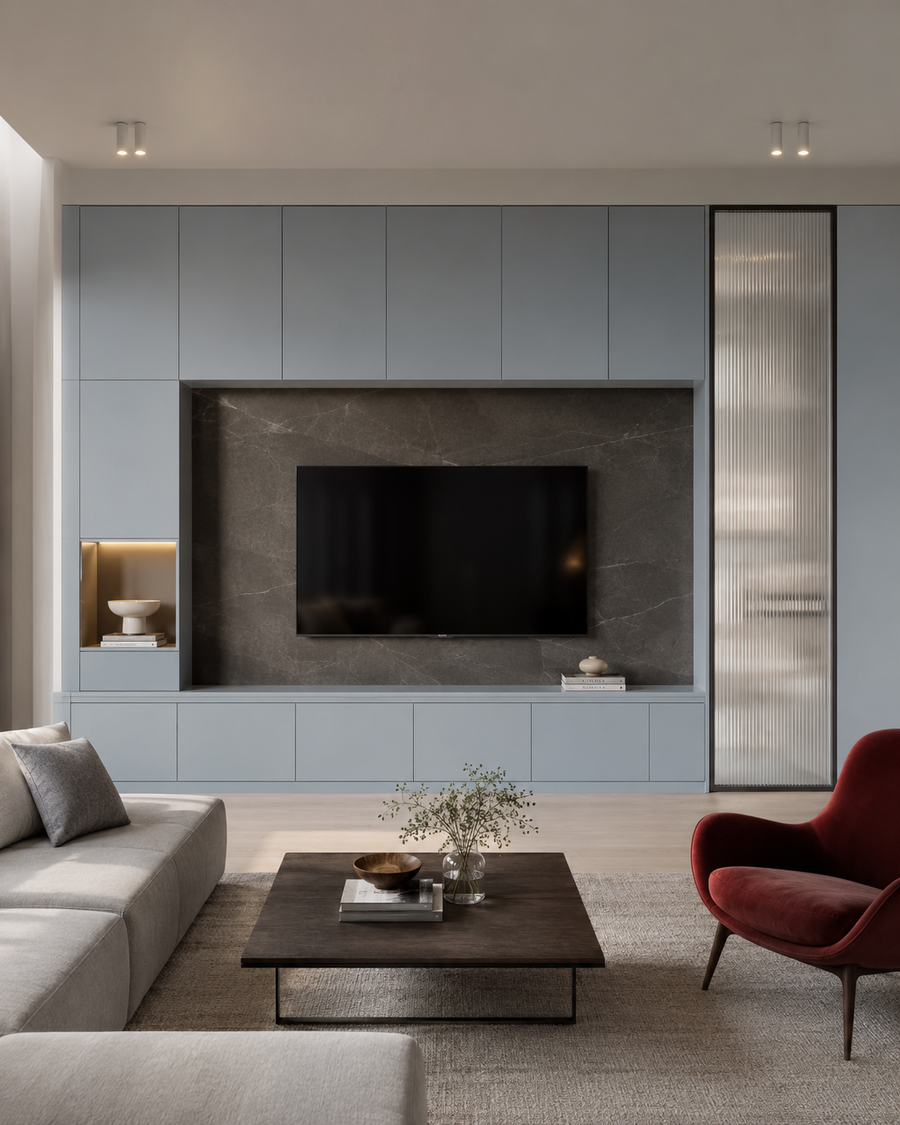 Front-facing Stockholm-modern media wall with pale blue-gray full-width cabinetry, a dark stone TV recess, concealed storage drawers, a reeded glass tall cabinet, and a red accent chair.