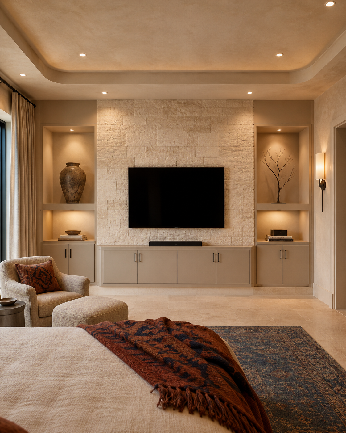 Front-facing bedroom media wall with a textured light limestone veneer TV panel, taupe lower cabinetry, illuminated side niches, and warm rust and indigo textiles.