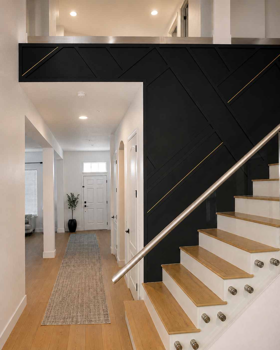Entry and staircase detail of a Winter Park accent wall project with black geometric paneling, glass railing, wood treads, and gold accent lines.