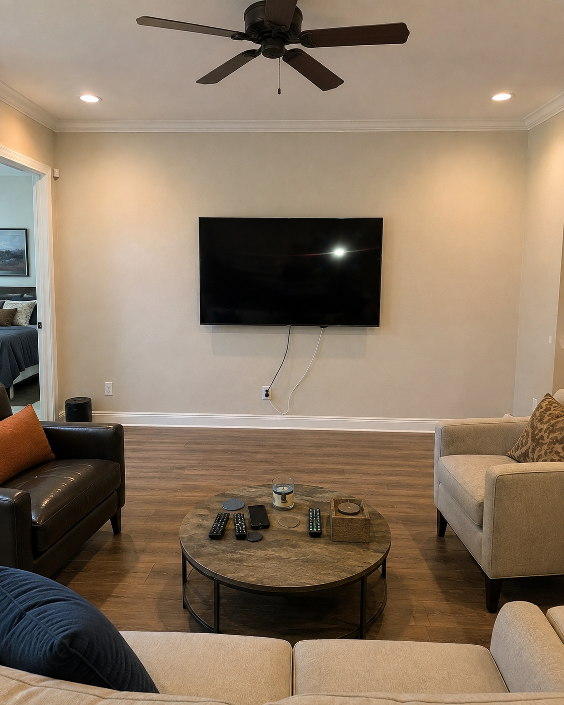 Before view of the Fort Myers living room showing a plain wall with a mounted TV and visible cords before the custom fireplace TV wall, stone surface, built-in storage, and lighted shelves were added.