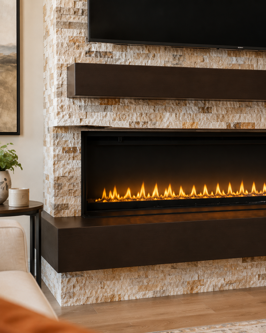 Detail view of the Jacksonville Custom Fireplace TV Wall showing warm-toned natural stone, the dark-stained wood mantel, the linear electric fireplace, and the projecting stained wood lower podium.