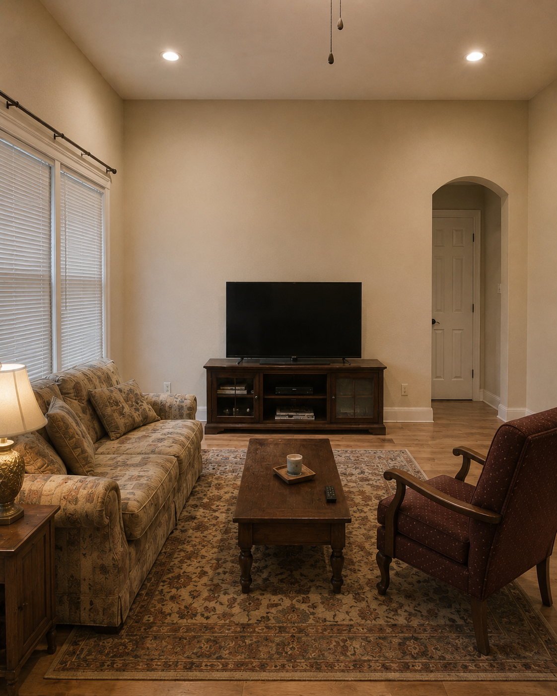 Before view of the Lake Mary living room with a plain wall, TV on a freestanding console, arched opening on the right, and no custom fireplace wall or ceiling beams.