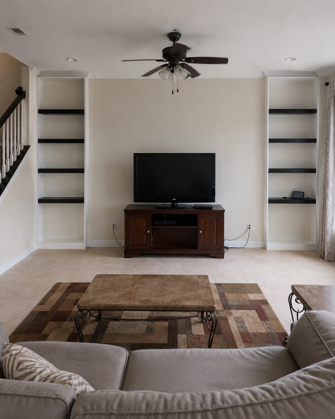 Before view of the Lake Nona living room with a plain center wall, TV on a freestanding console, existing side alcoves and shelves, and no new fireplace wall, lower cabinets, stone backing, or integrated lighting.