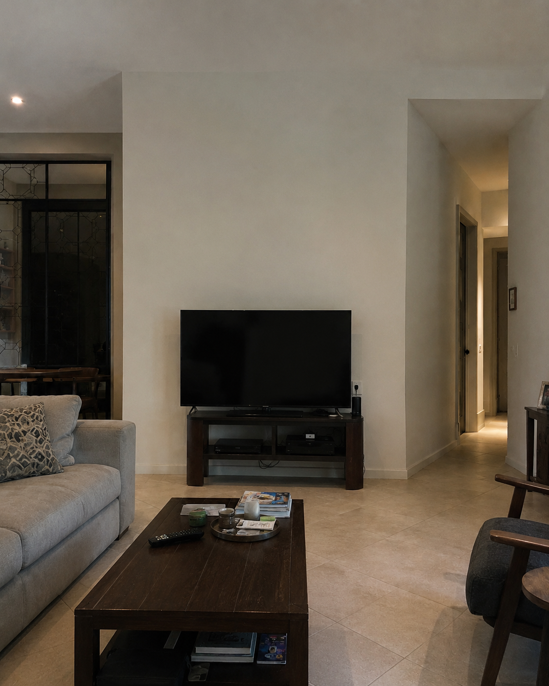 Before view of the Oviedo living room showing a TV on a freestanding media console against a plain wall between the exterior-door opening on the left and the hallway opening on the right.